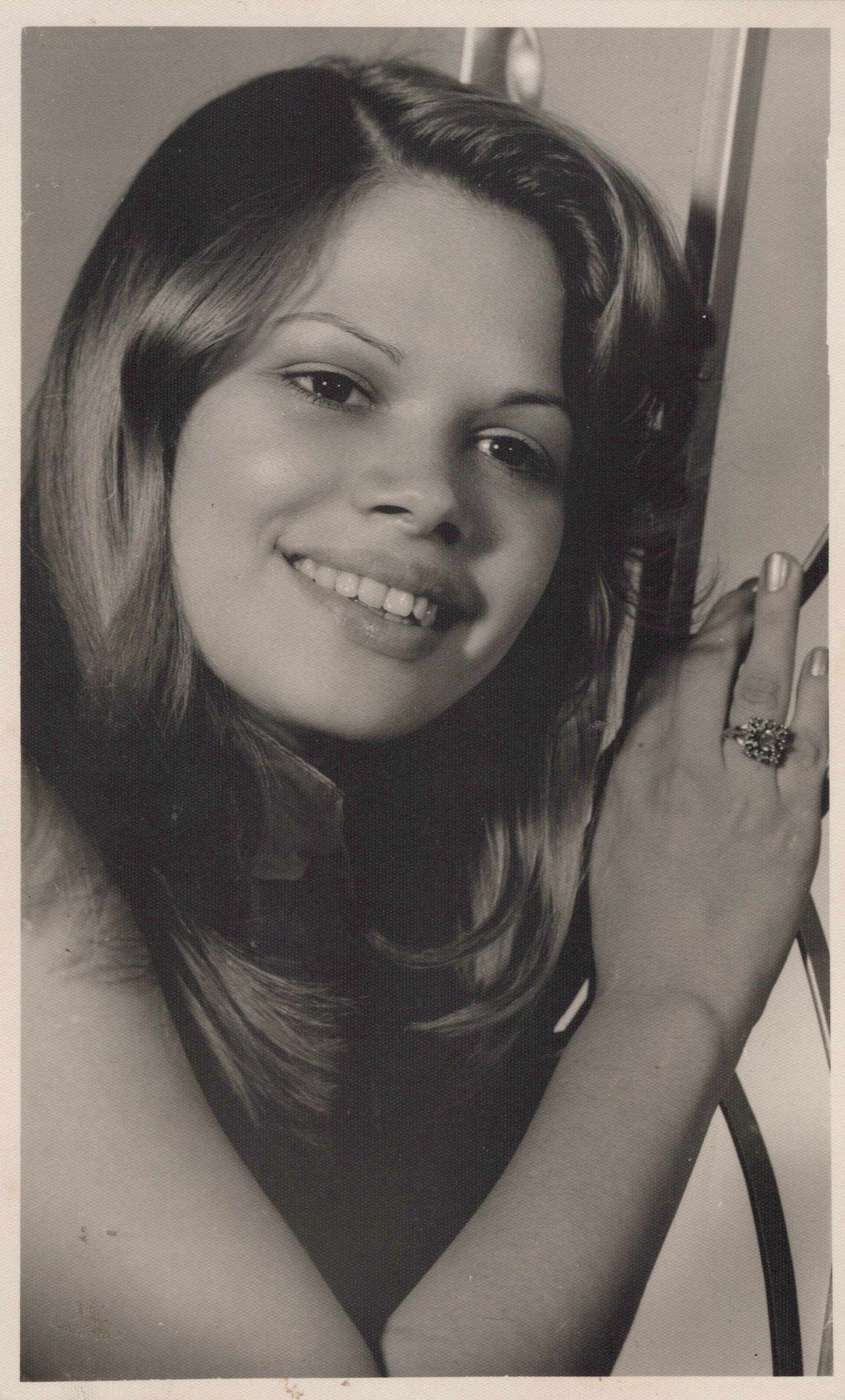 Black-and-white close portrait of Xiomara smiling with her hands raised near her face.