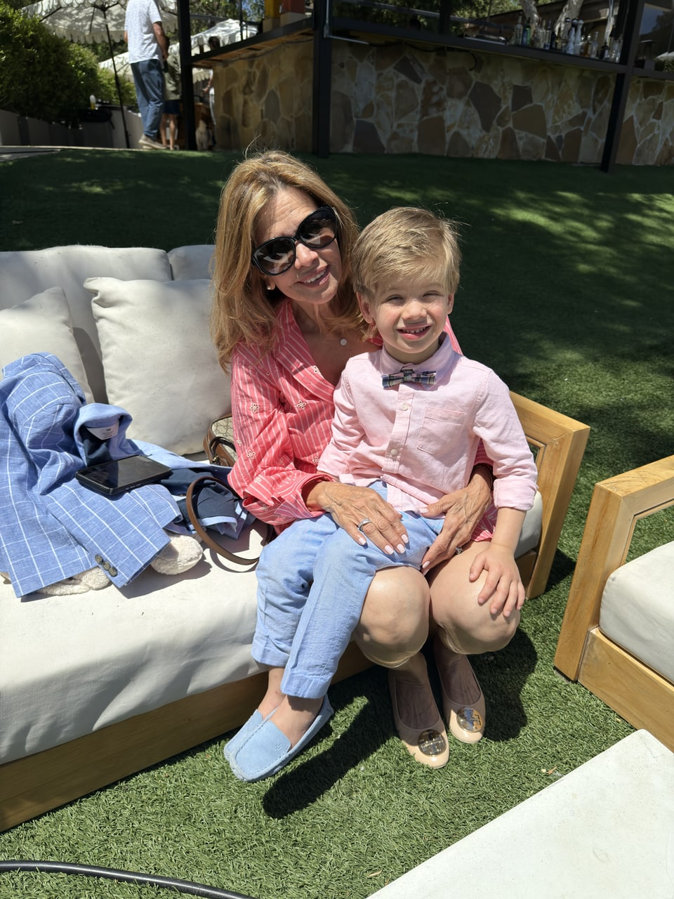 Xiomara in sunglasses sits outdoors with a smiling young boy on her lap.