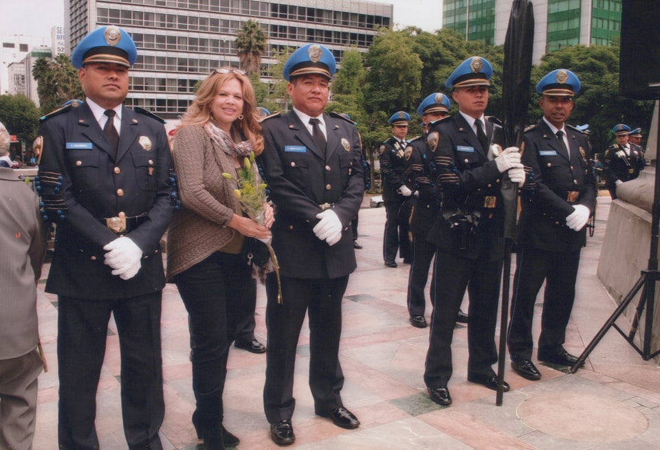 Xiomara holds flowers while standing among uniformed people outdoors.