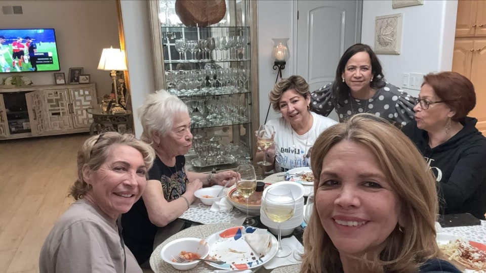 Xiomara smiles in the foreground of a group gathered around a dining table.
