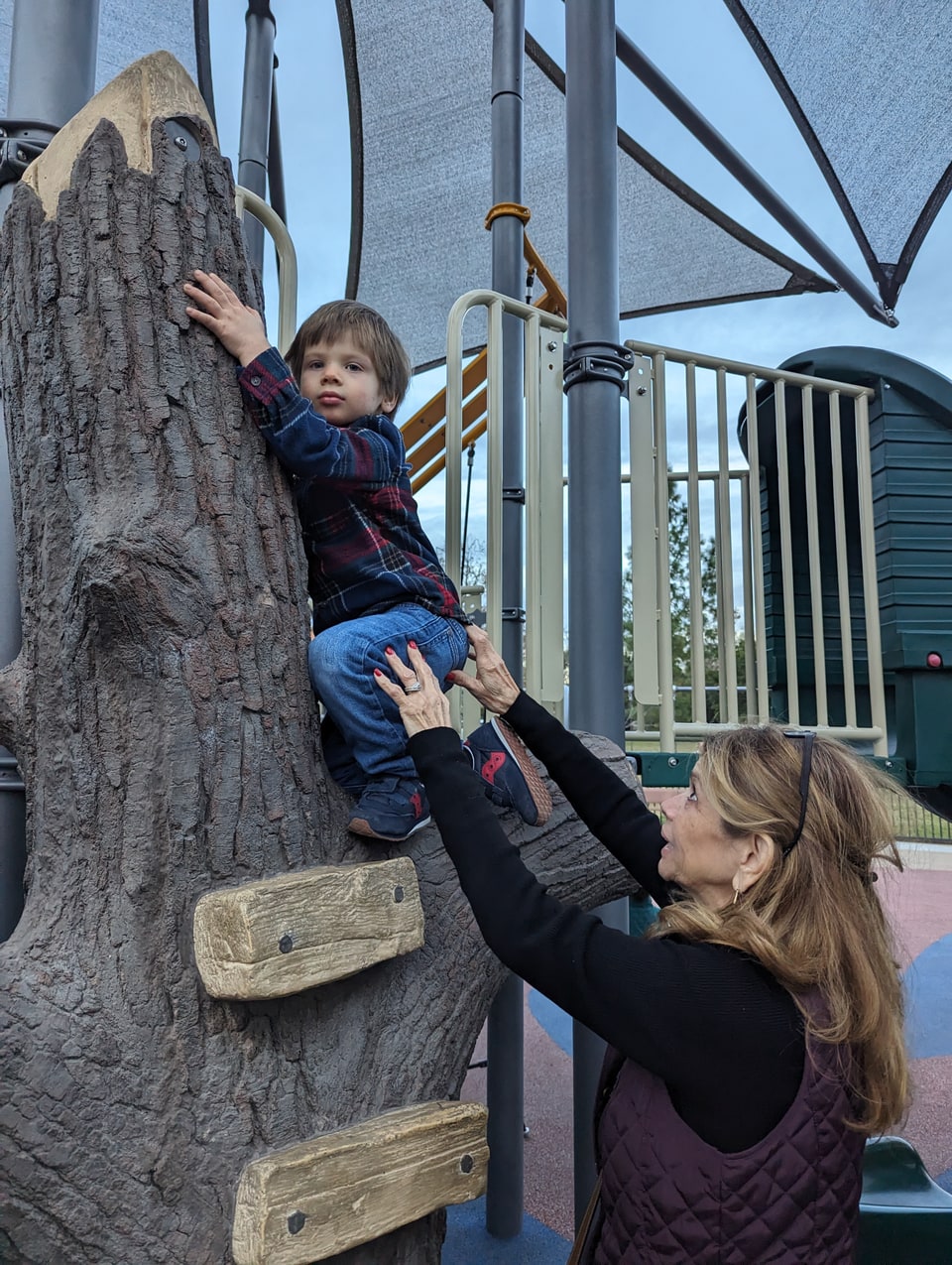Xiomara reaches up to steady a young boy climbing a playground structure.