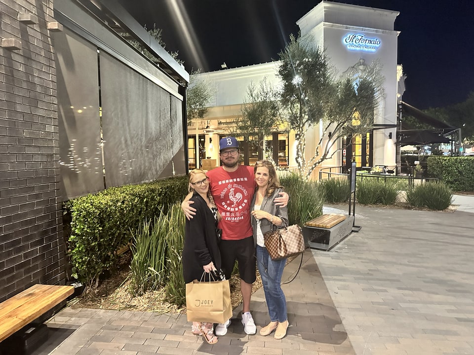 Xiomara stands with two people outside a brightly lit restaurant at night.