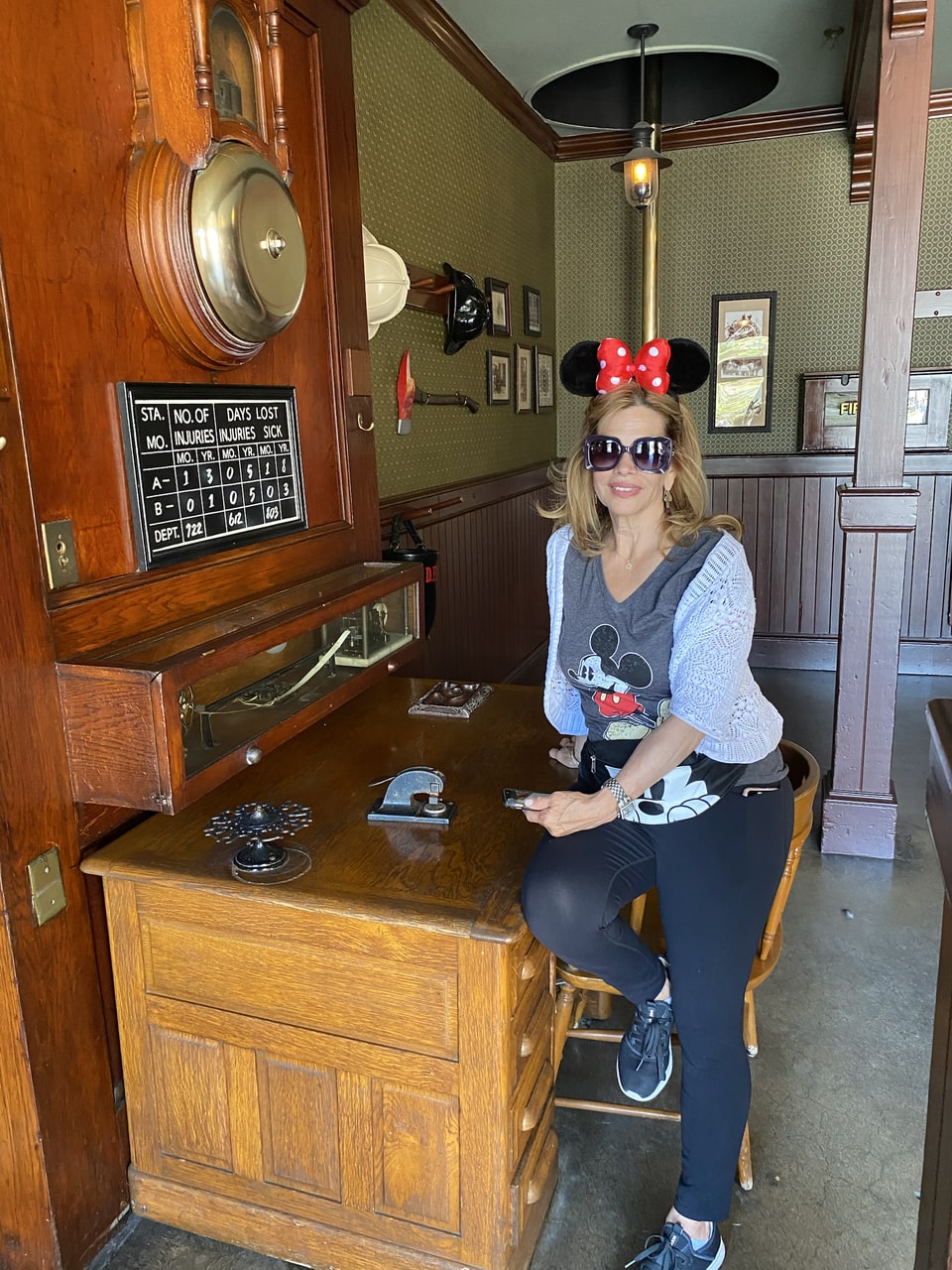 Xiomara poses in sunglasses and a red bow headband beside an antique wooden machine.
