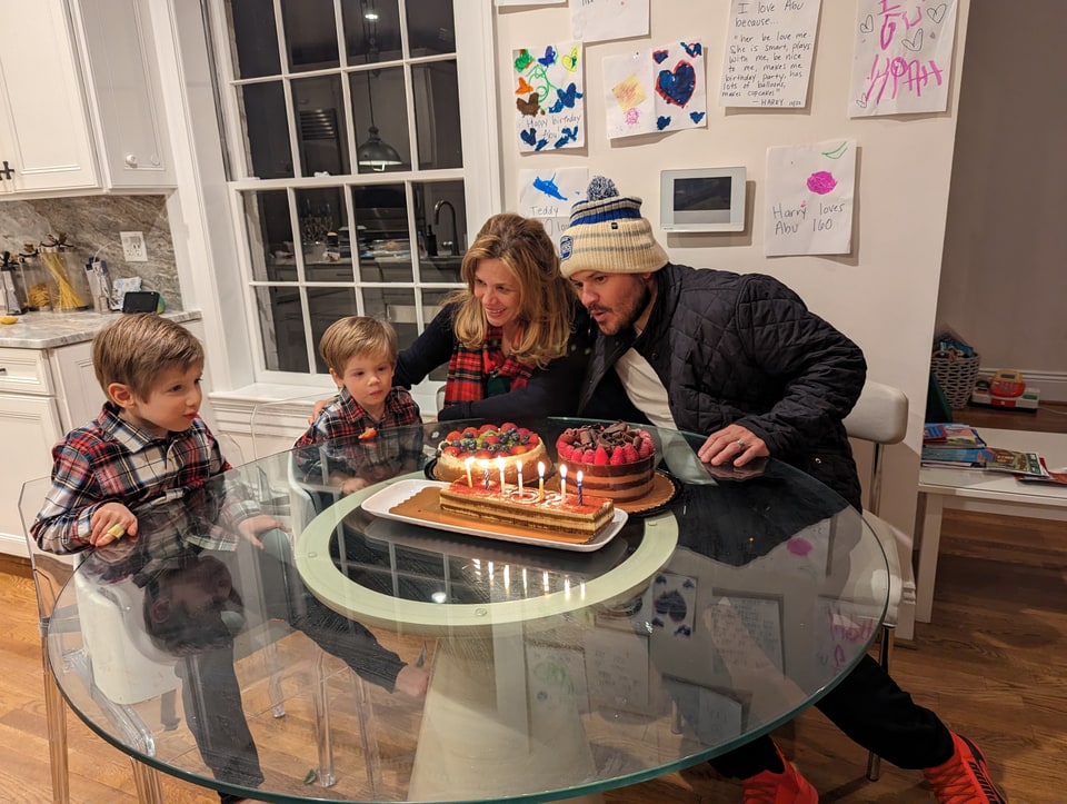 Xiomara smiles with an adult and two young boys gathered around cakes with lit candles.